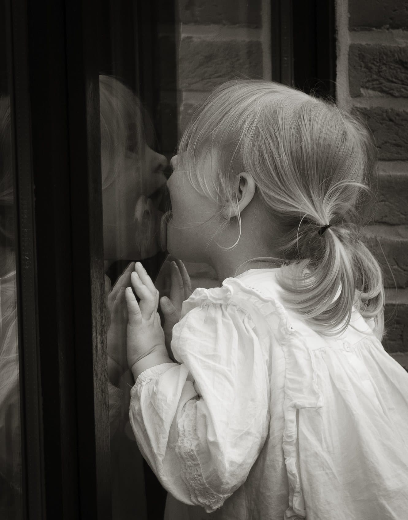 Tout-petit écrasant son visage et ses mains contre une vitre, son reflet visible