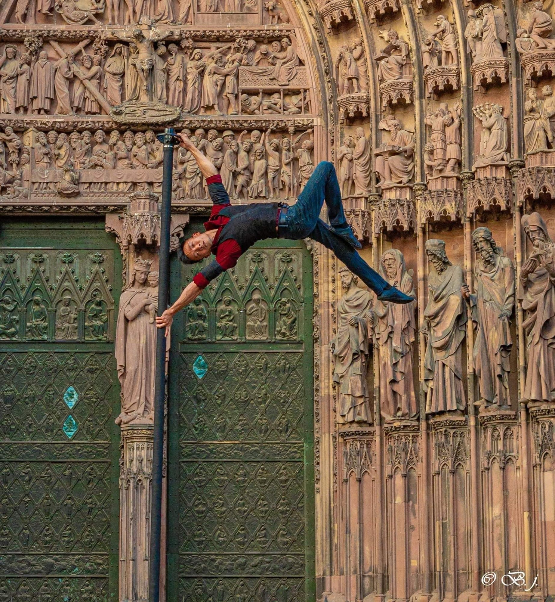Acrobate de rue à l'horizontale sur un mât devant le portail de la cathédrale