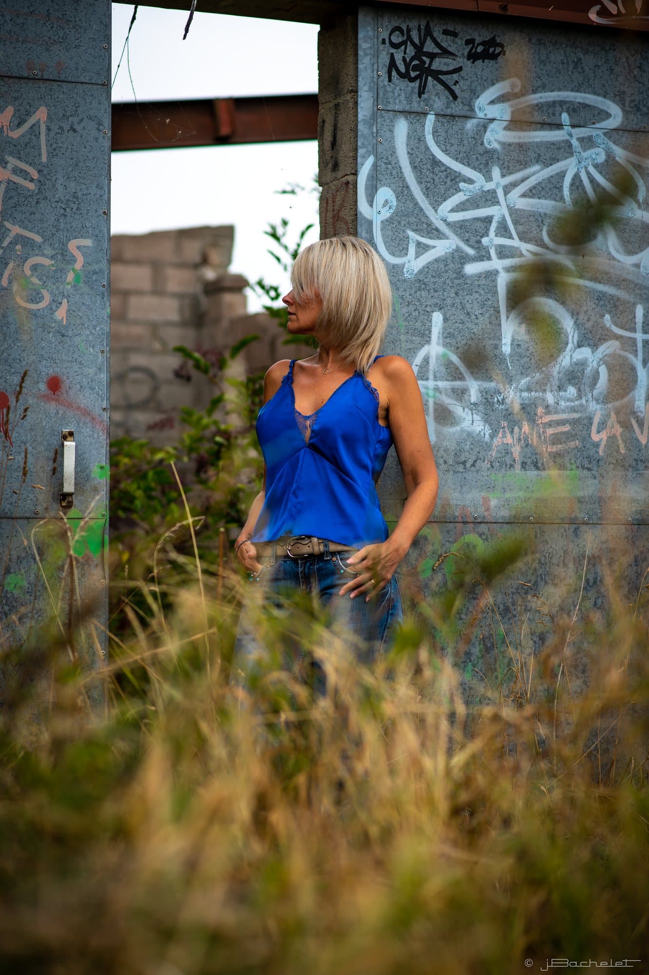 Femme en caraco de soie bleue devant un mur de ruine couvert de graffitis