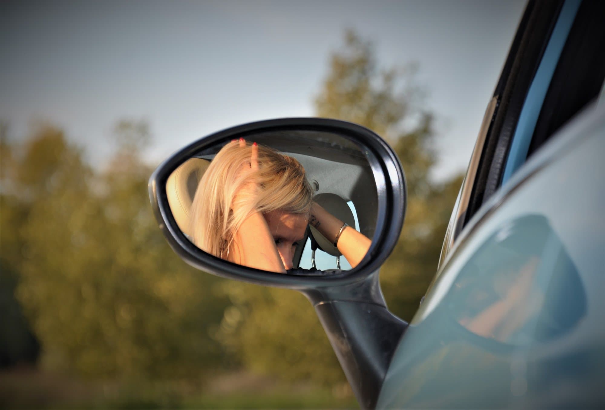 Femme reflétée dans le rétroviseur d'une voiture, arbres à l'heure dorée