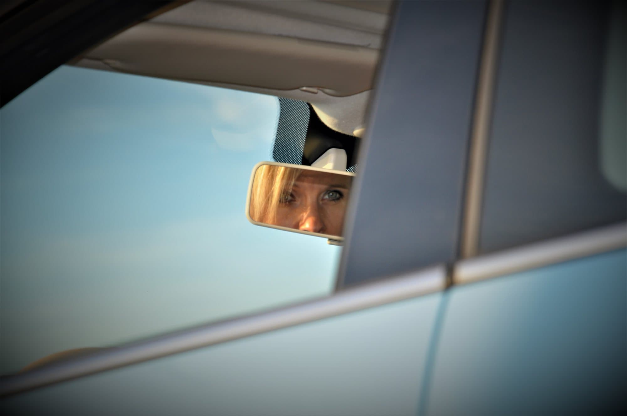 Yeux d'une femme saisis dans un rétroviseur intérieur, ciel bleu