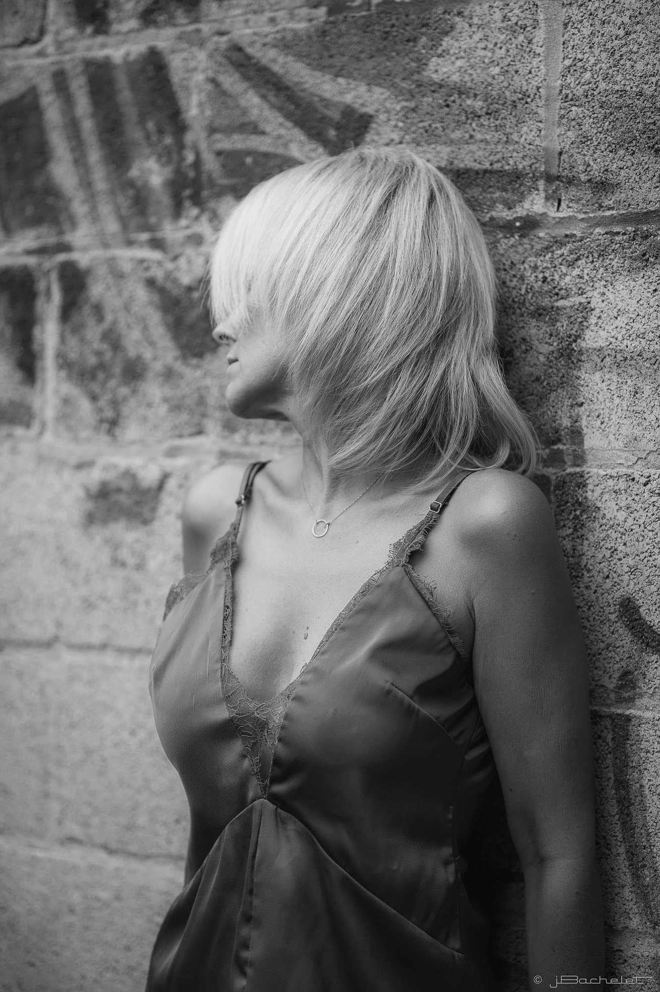 Femme en nuisette de satin appuyée à un mur de pierre, les cheveux sur le visage